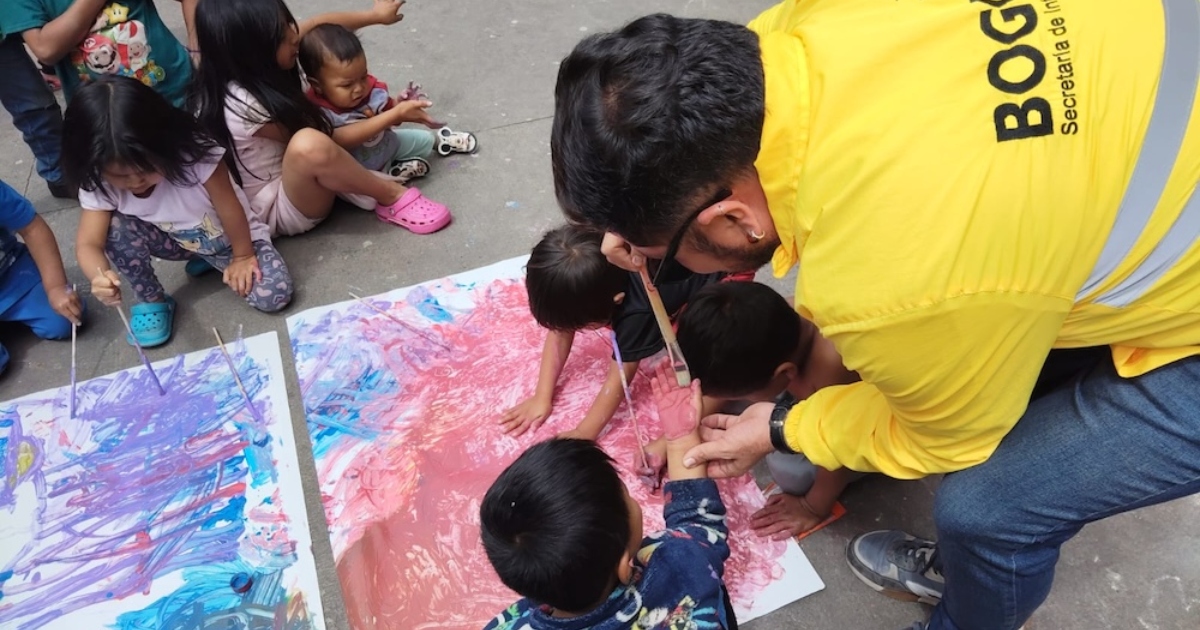Imagen de un funcionario de Integración Social ayudando a niños y niñas Emberá a pintar.