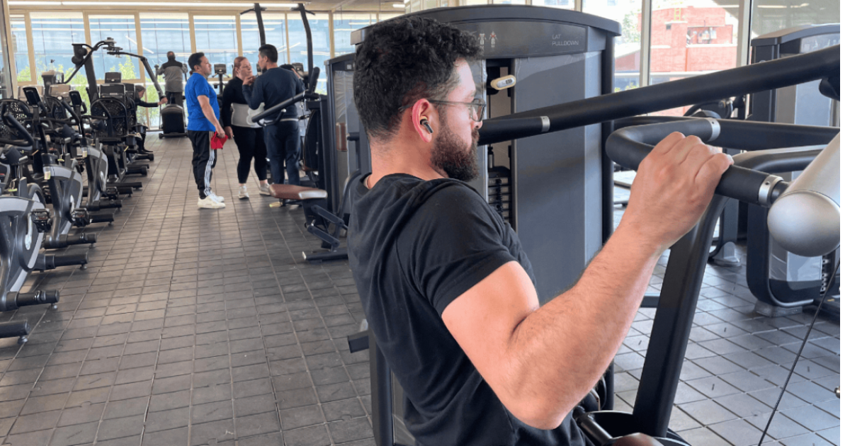 Imagen de hombre haciendo ejercicio en máquina, al fondo se ven más personas ejercitándose