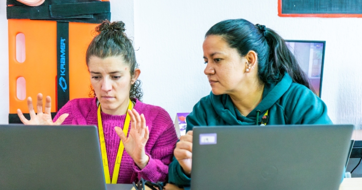 Foto que muestra dos mujeres hablando y trabajando frente a un computador