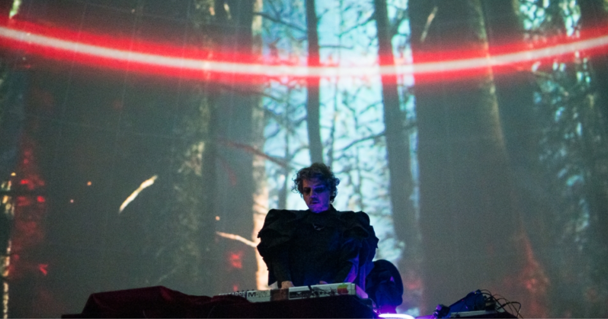 Imagen de un dj tocando en su tornamesa, de fondo se ve la imagen de un bosca iluminado con una luz roja de lado a lado.