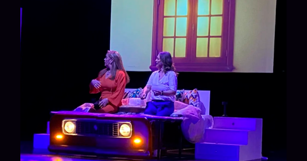 Imagen de dos mujeres mayores sentadas en un sofá en la sala de una casa hablando alegremente, de fondo se ve una venana