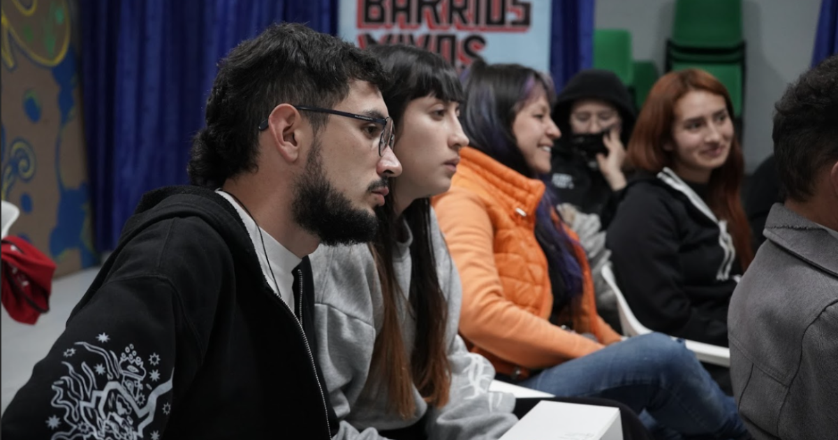 Imagen de varias personas, que sentadas prestan atención a alguien que esta de frente. 