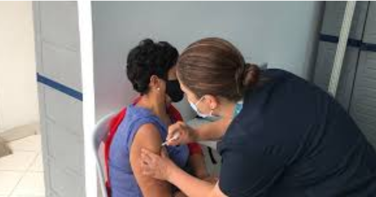 Imagen de una enfermera aplicando una vacuna a una mujer de mediana edad que usa tapabocas