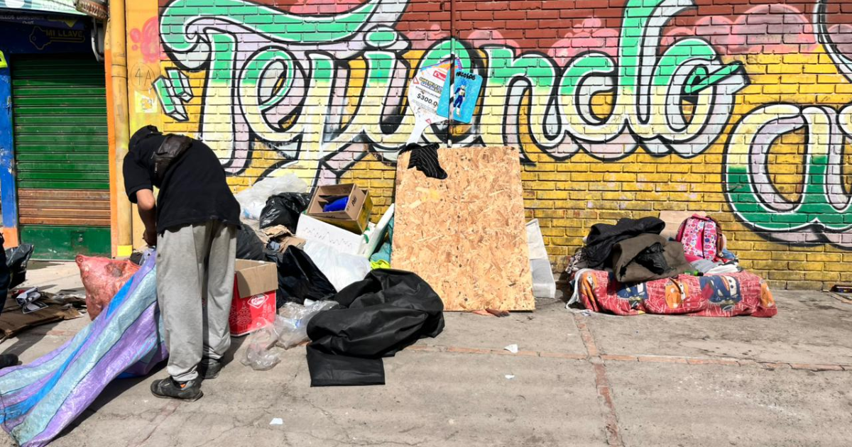 Foto de una persona que organiza pertenencias y materiales en medio de residuos acumulados junto a un muro