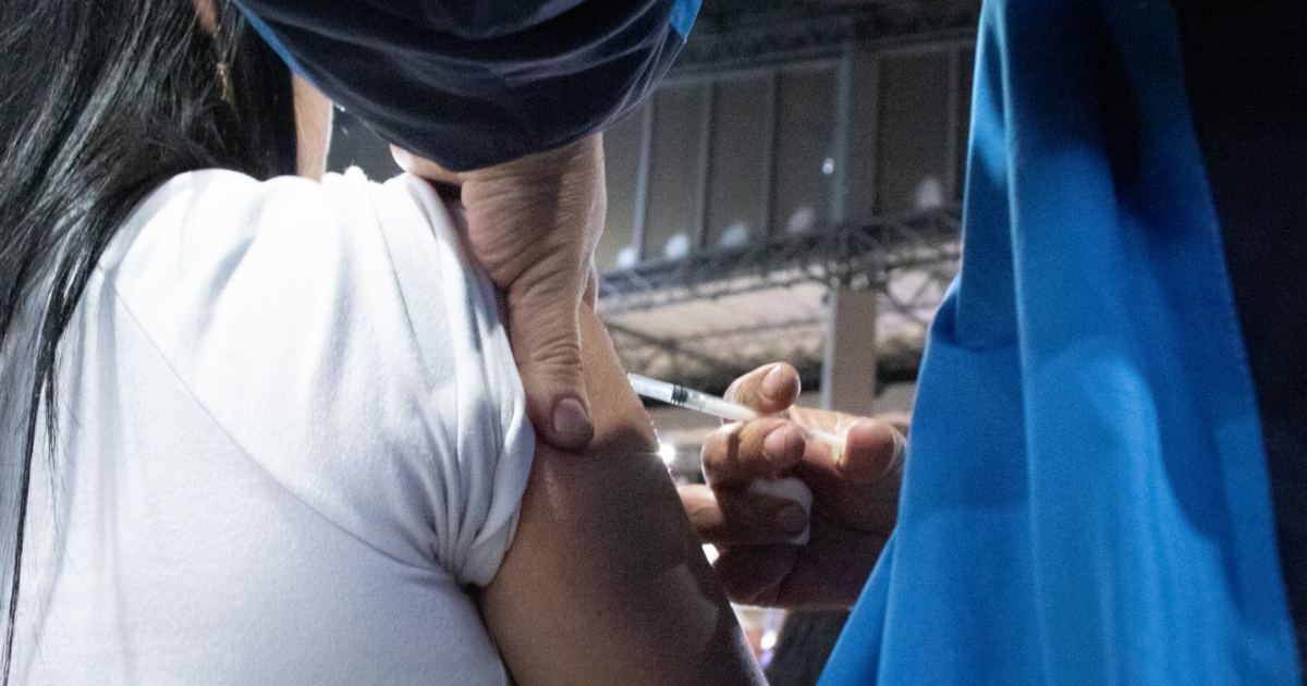 Imagen de una enfermera aplicando una vacuna a una mujer de mediana edad que usa tapabocas