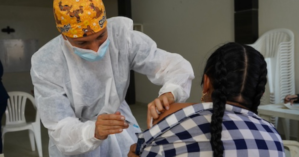 Imagen de enfermera que coloca vacuna a una mujer que está sentada.