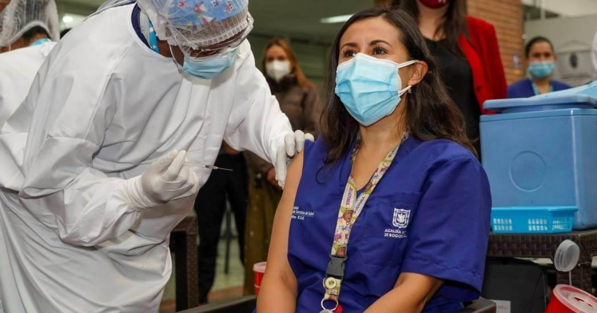Imagen de mujer sentada y junto a ella una enfermera la vacuna