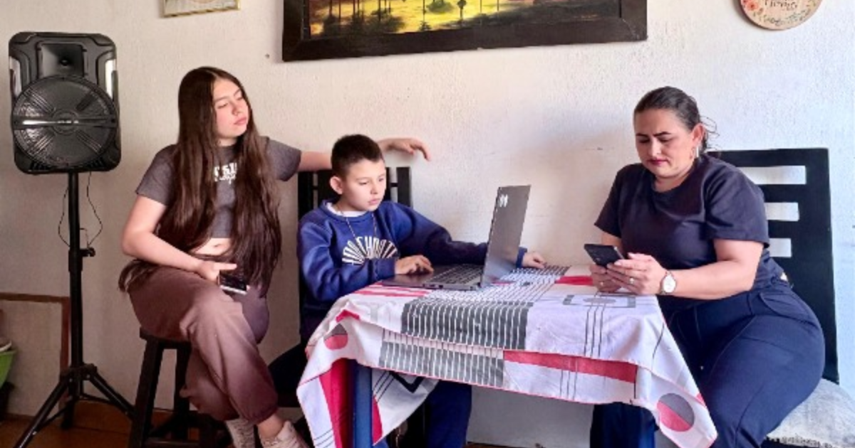 Imagen de una madre de familia con su hijo e hija estudiando en un computador