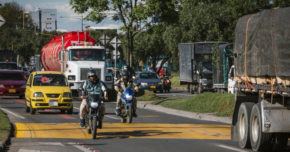 Imagen panoramica de una vida principal de Bogotá en la que se observan las demarcaciones de tránsito y en la que circulan buses, vehíclos particulares y taxis.