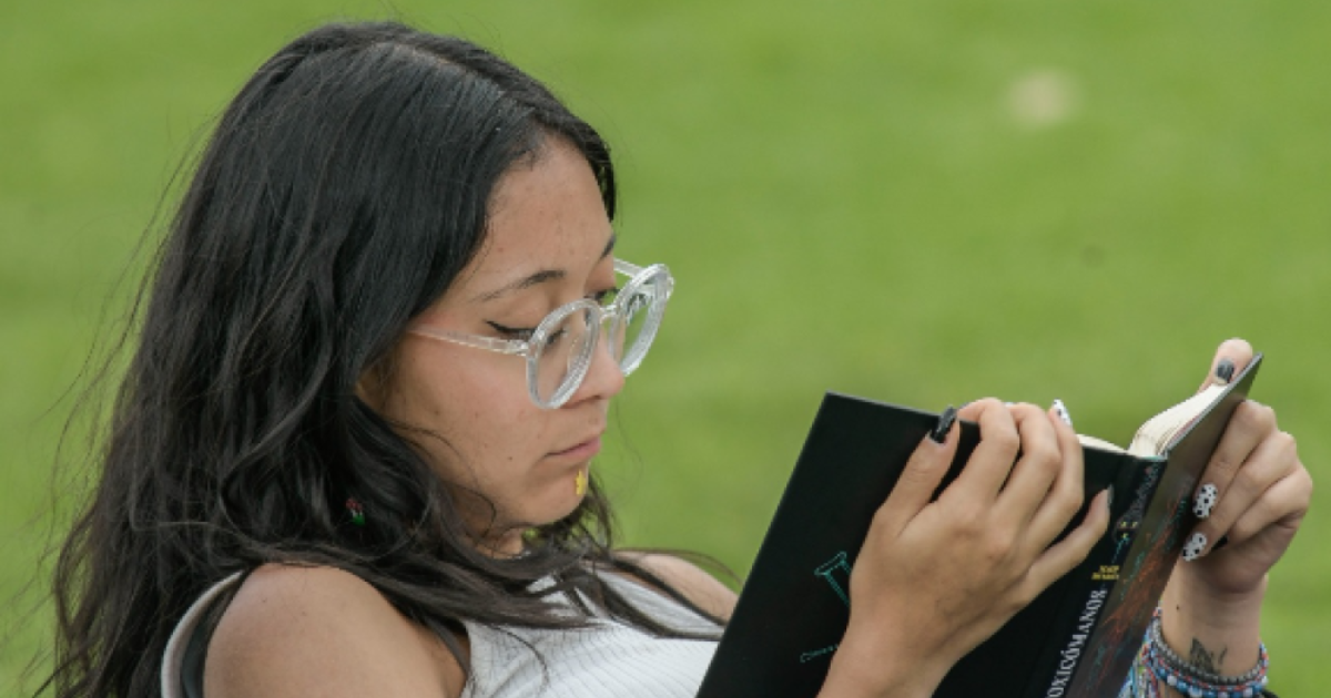 Imagen de una mujer leyendo un libro, sentada comodamente en un parque.