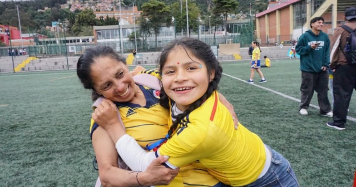 Imagen de una madre junto a su hija quien la abraza y sonríe