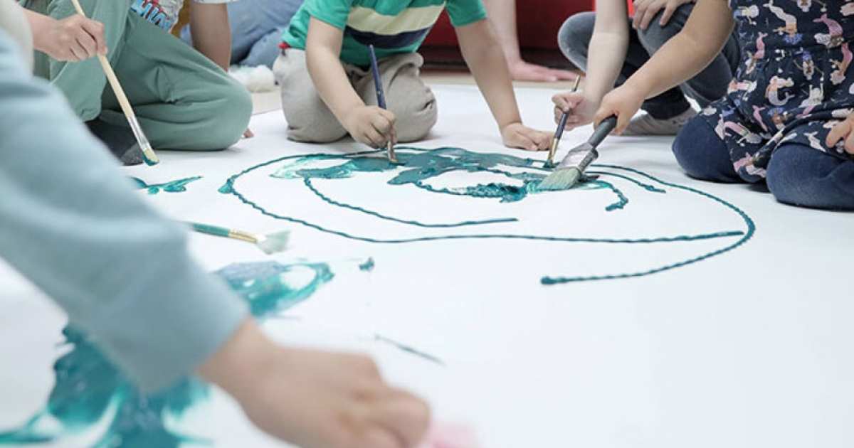 Foto que muestra niños y niñas con pintando en una cartulina con pinceles y pinturas 