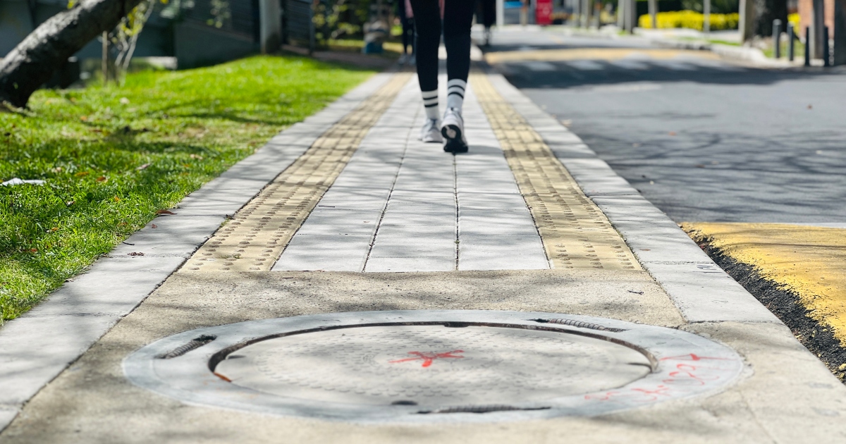 Foto que muestra una persona caminando por un andén en el que se ve una tapa de alcantarillado