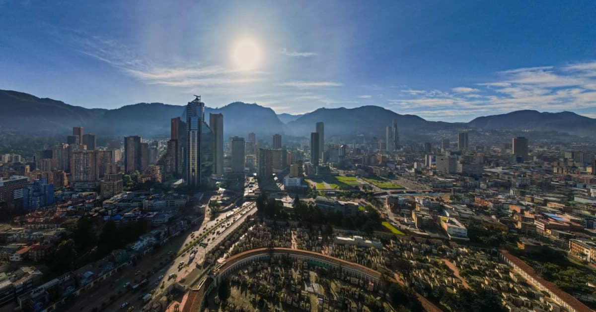 Vista panorámica de Bogotá con vista a edificios, montañas, cielo despejado y sol intenso