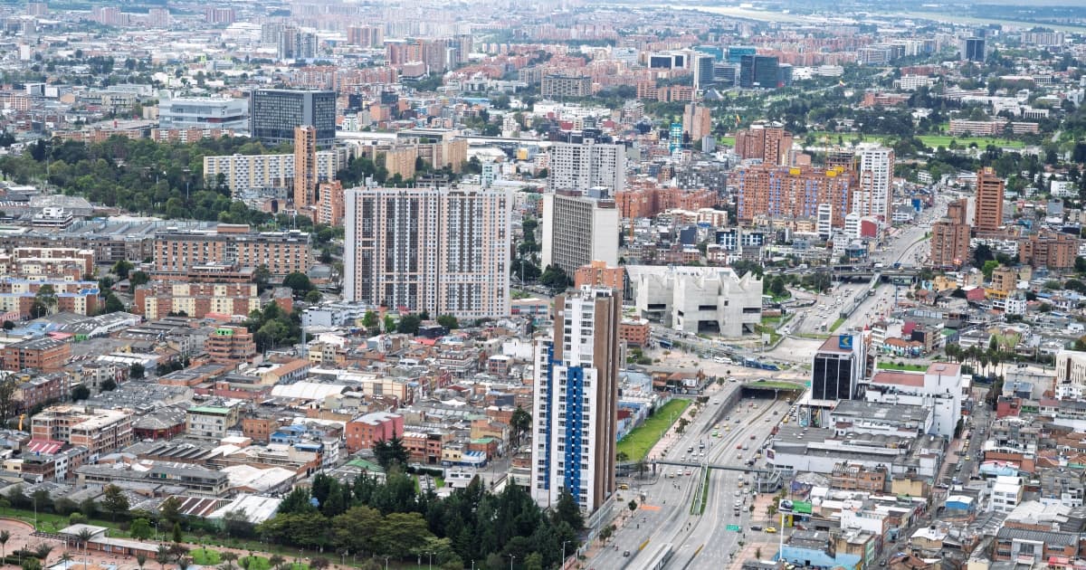 Vista aérea de Bogotá con edificaciones, avenidas principales y zonas verdes en día nublado.