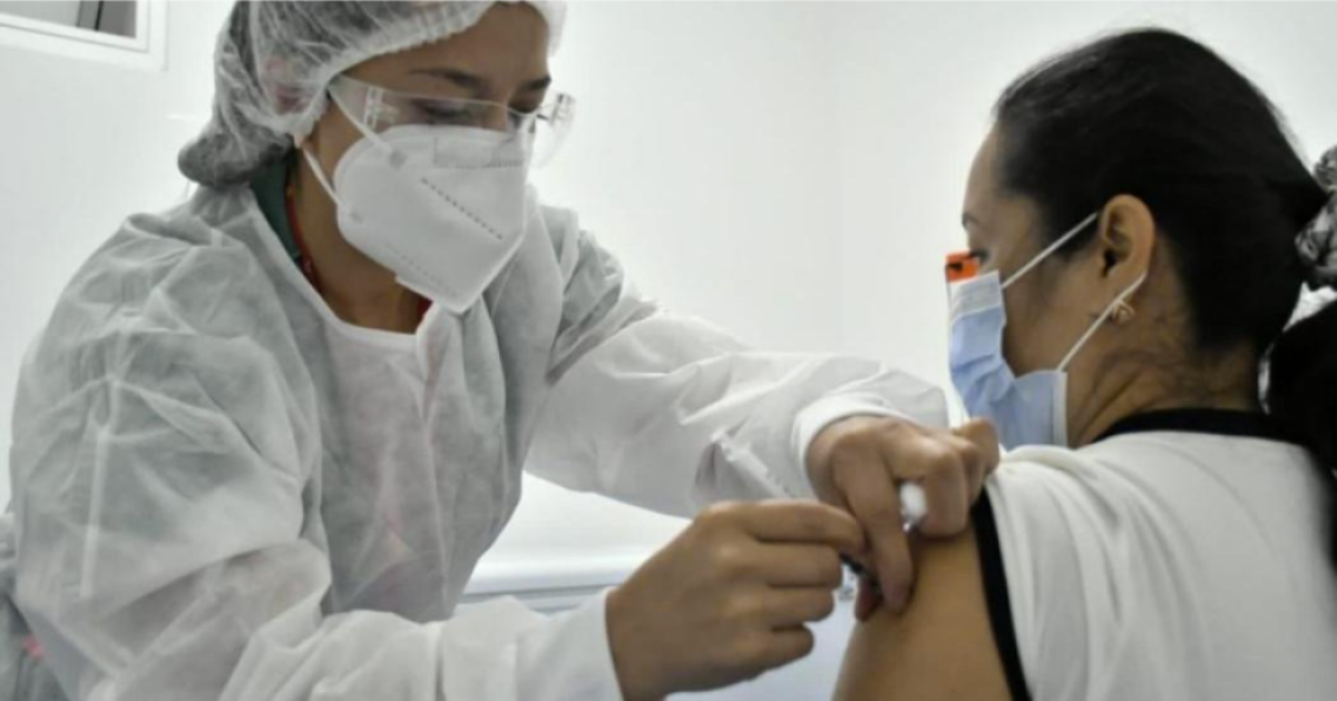 Imagen de una enfermera aplicando una vacuna a una mujer de mediana edad que usa tapabocas