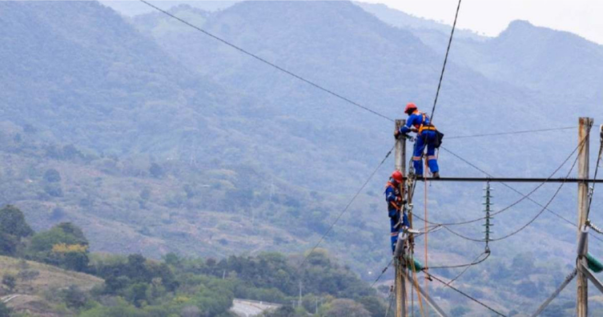 Imagen dos técnicos de Enel realizando mantenimiento a un poste de luz, de fondo se ve la ciudad.