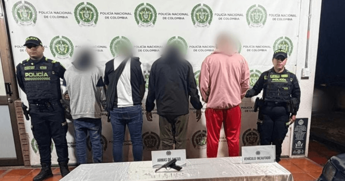 Cuatro capturados en medio de dos policías. El arma incautada está sobre una mesa.