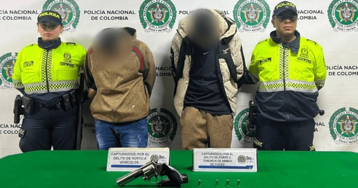 Dos capturados en medio de dos Policías. Sobre una mesa está el arma y los car