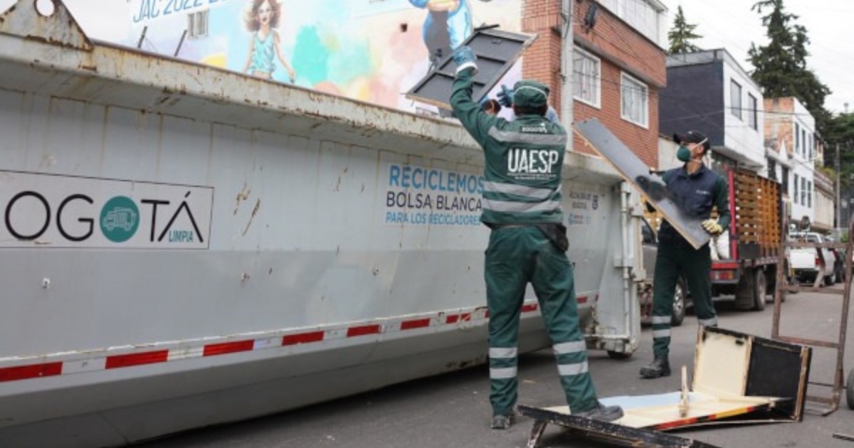 Foto que muestra dos personas dejando residuos en un carro recolector