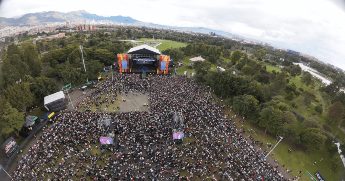 Vista aérea de concierto masivo en el parque Simón Bolívar con miles de asistentes reunidos frente a un escenario principal rodeado de zonas verdes y árboles.