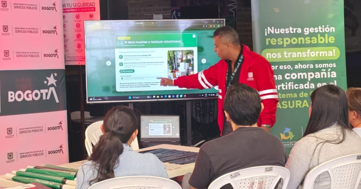 Foto que muestra personas sentadas y un señor señalando un televisor 