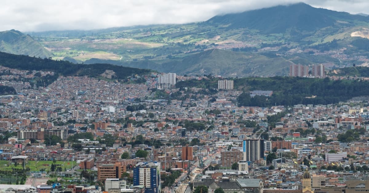 Panorámica de Bogotá con barrios densos, cerros verdes y cielo nublado fondo