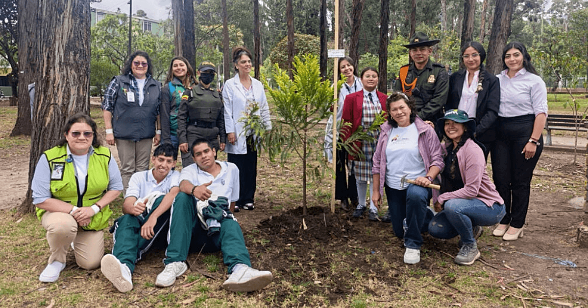 Grupo de personas participa en una jornada de siembra de árboles y arbustos en el Bosque Urbano San Carlos, junto a ejemplares recién plantados y rodeados de vegetación y árboles.