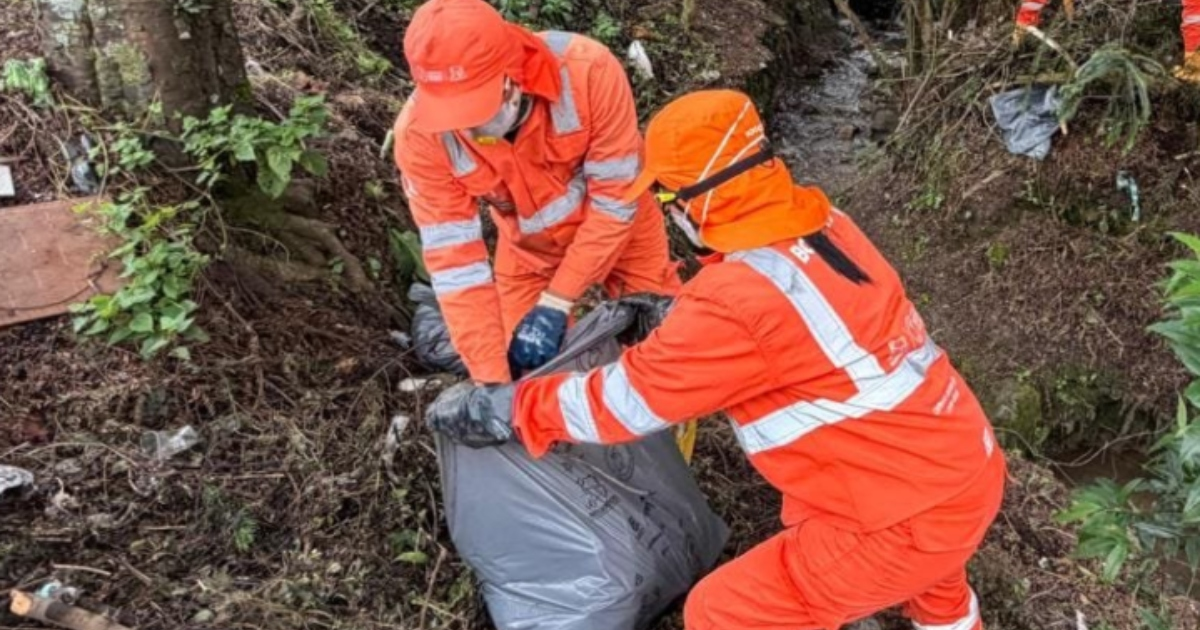 Foto que muestra dos personas levantando una bolsa con residuos 