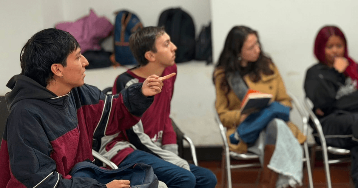 Foto que muestra dos hombres y dos mujeres sentados en escritorios dentro de un salón