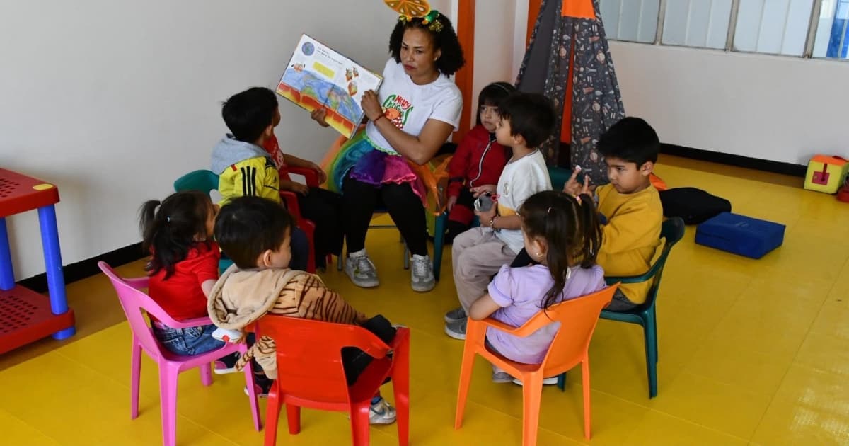 Niños en mesa redonda leyendo un libro con una profesora 