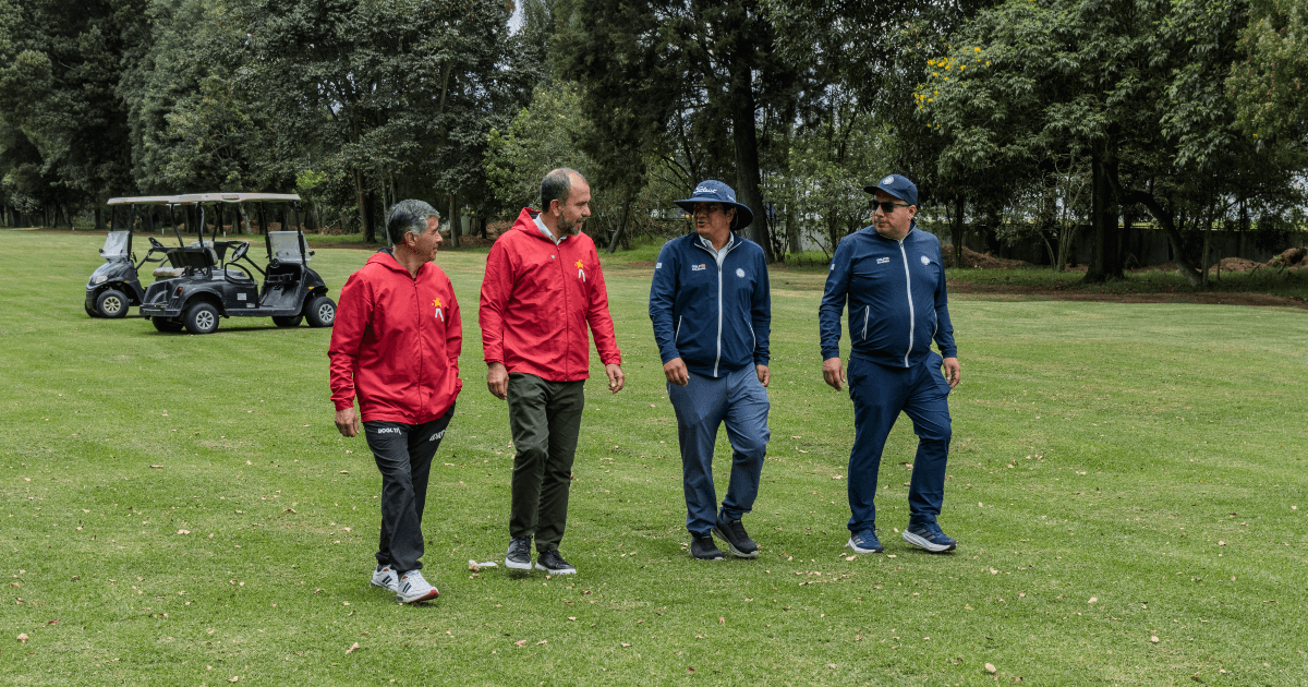 Cuatro personas caminan sobre el césped del campo de golf del Parque La Florida. Dos visten chaquetas rojas y dos chaquetas azules.