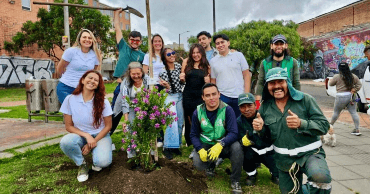 Grupo de personas posa alrededor de un arbusto con flores moradas recién sembrado en una zona verde.