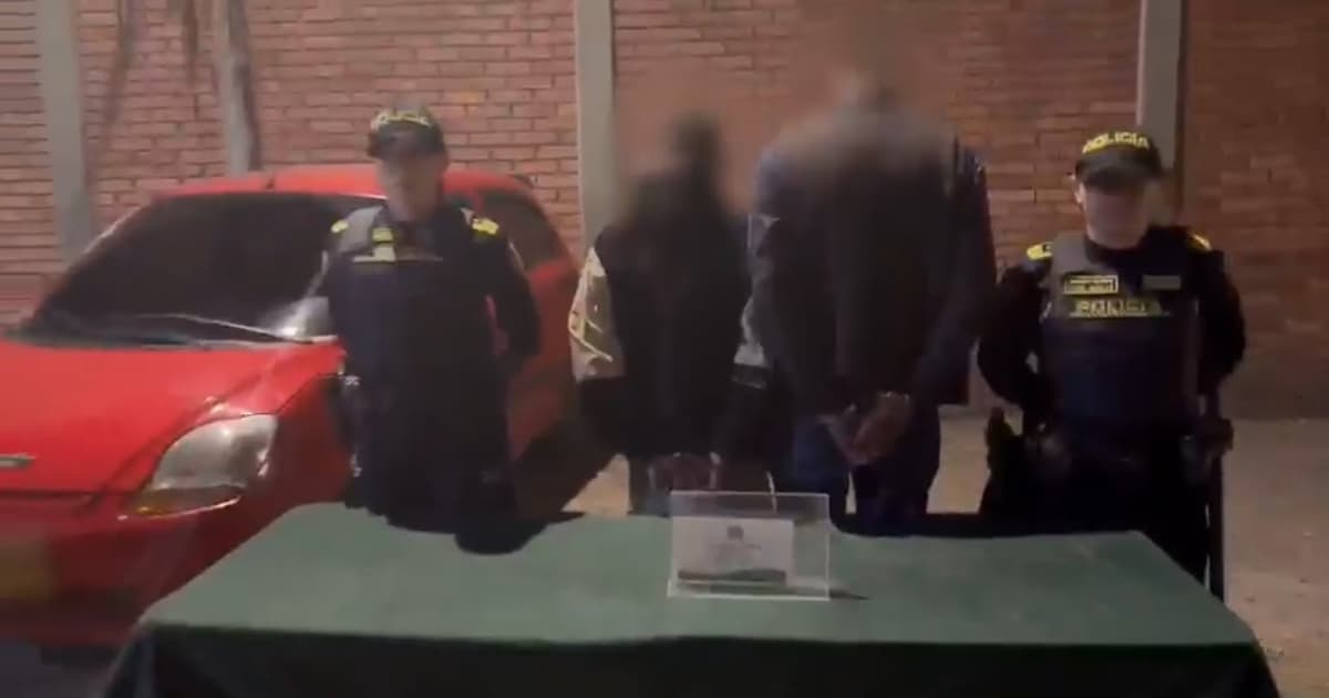 Dos personas capturadas de espaldas y esposados junto a dos policías 