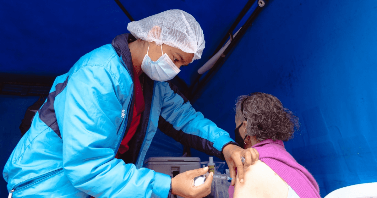 Foto que muestra una persona con gorro y tapabocas colocando una vacuna 