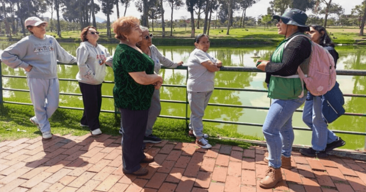 Participantes de una jornada comunitaria de siembra en el parque Timiza sostienen herramientas y materiales de jardinería junto a un área verde delimitada para la plantación de árboles y arbustos.