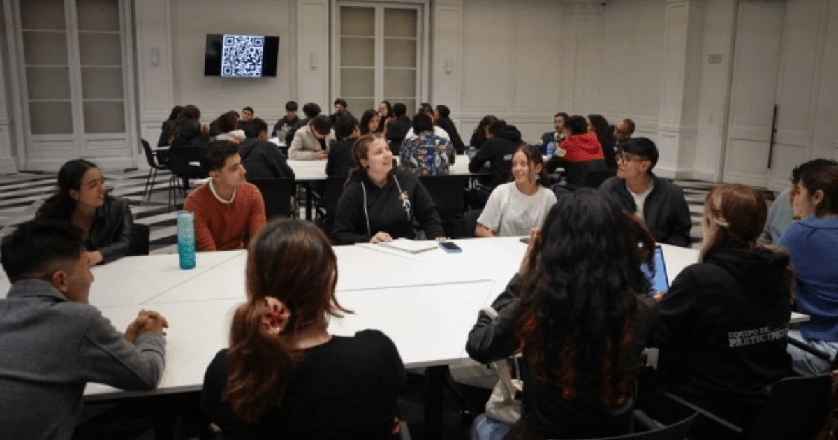 Foto que muestra estudiantes sentados en una mesa hablando 