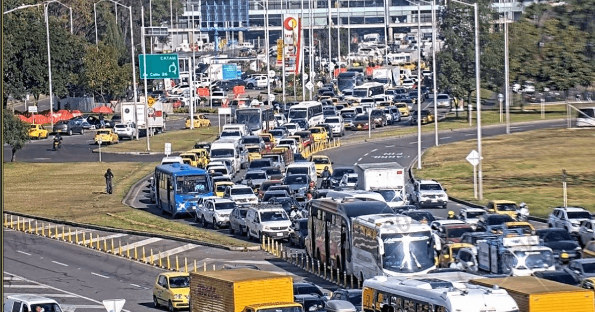 Alta congestión vehicular en avenida El Dorado de Bogotá con filas de carros, buses, camiones y motocicletas avanzando lentamente entre varios carriles. Se observan separadores viales, señalización y tránsito denso en ambos sentidos.