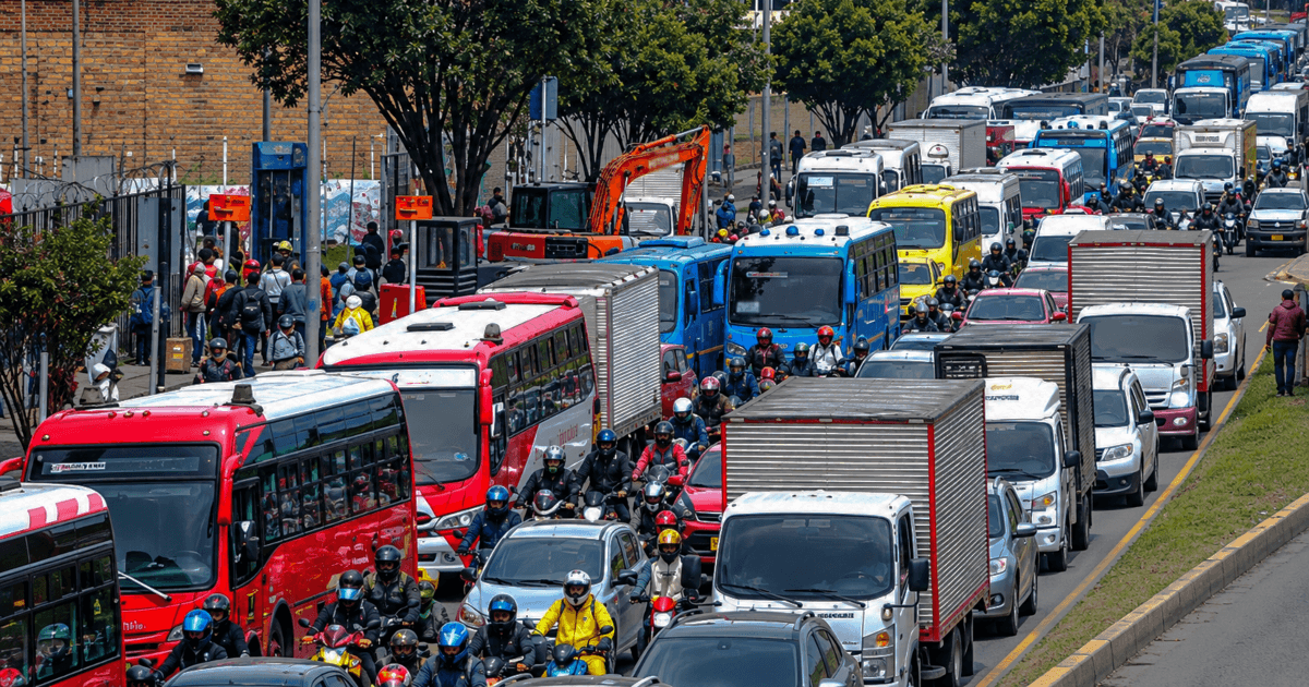Tráfico congestionado sobre una avenida de Bogotá, con buses de TransMilenio, vehículos particulares, camiones y numerosas motocicletas ocupando varios carriles.
