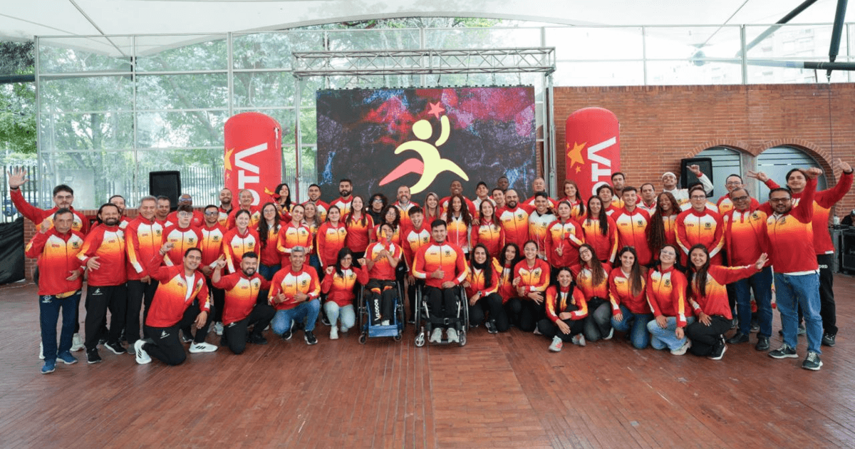 Grupo de deportistas del Equipo Bogotá posa para una foto durante un homenaje, frente a una pantalla con el logo de los Juegos Suramericanos y elementos de escenografía institucional.
