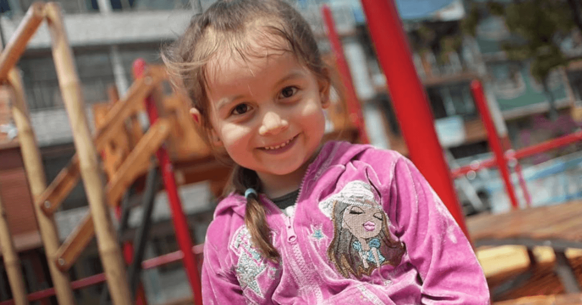 Foto de una niña sonriente con un saco rosado.