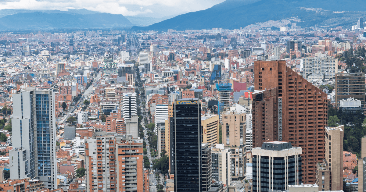 Vista panorámica del centro de Bogotá con edificios de gran altura, zonas residenciales densamente construidas y montañas al fondo bajo cielo parcialmente nublado.