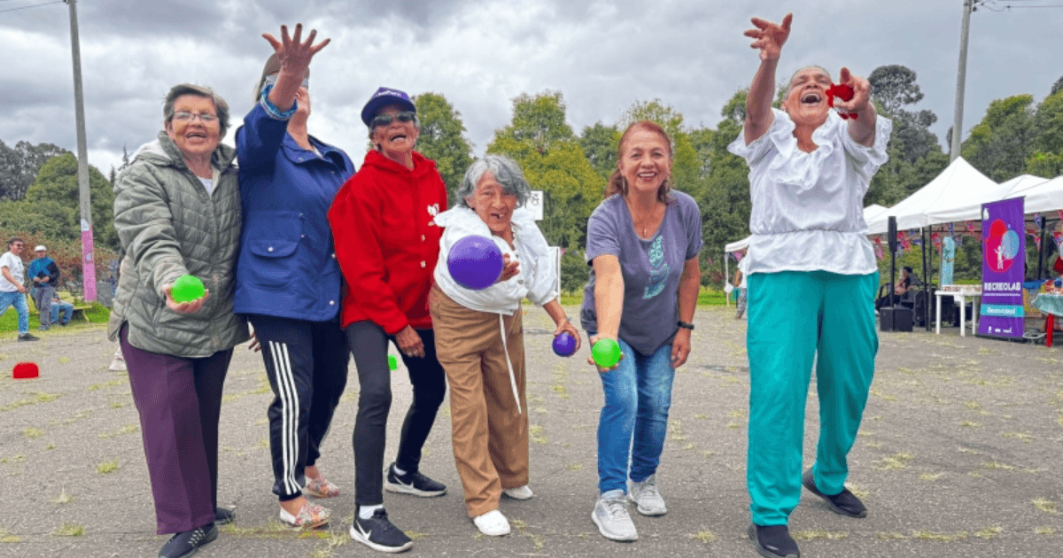 Grupo de personas participa en una actividad recreativa al aire libre; varias sostienen pelotas mientras avanzan por una zona verde.