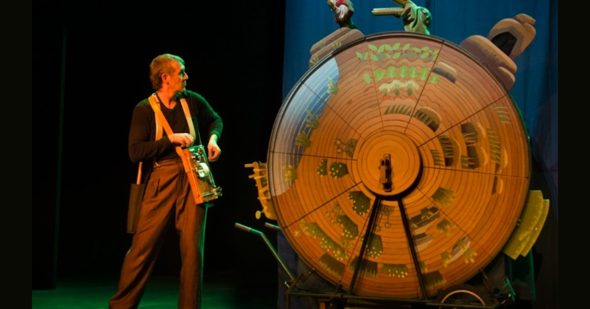 Imagen de un hombre frente a un relog de madera gigante alusivo a la obra de teatro 