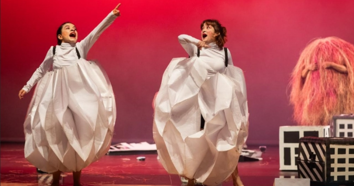 Imagen de dos mujeres jóvenes con trajes blancos y a su lado Burí, un personaje peludo de color rosado