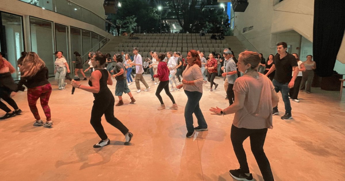 Imagen de un gran salón donde hay muchas personas tomando clases de baile 