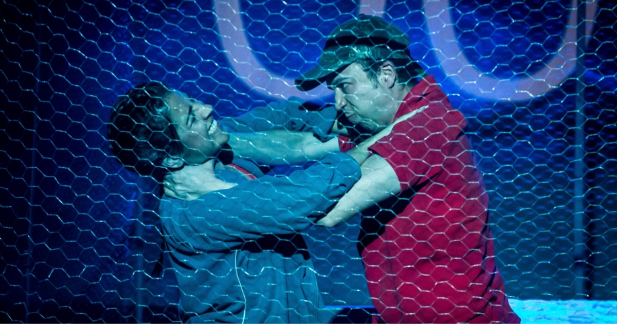 Imagen de dos hombres detrás de una cerca peleando, se aprecia como se aprietan el cuello