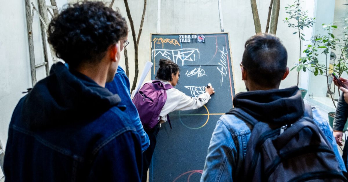 Imagen de personas reunidas al frente de un tablero con grafitis 
