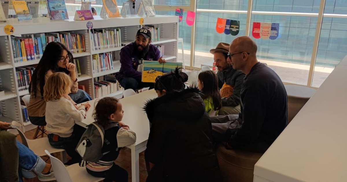 Foto que muestra un grupo de personas y niños sentados en un salón de una biblioteca