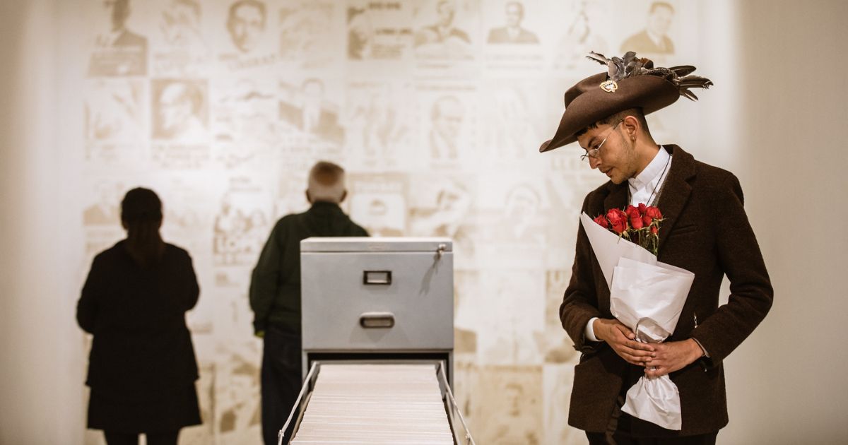 Imagen de uh hombre con sombrero y ramo de rosas mirando uno de artículos de la expo en la FUGA